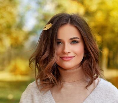 Portrait of beautiful autumn brunette woman with long wavy bob hairstyle smiling. Cute lady on a golden autumn background.