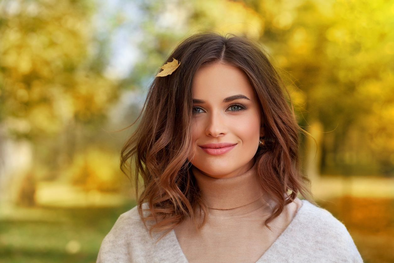 Portrait of beautiful autumn brunette woman with long wavy bob hairstyle smiling. Cute lady on a golden autumn background.