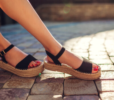 Stylish woman wearing black summer shoes with straw sole outdoors. Comfortable sandals.